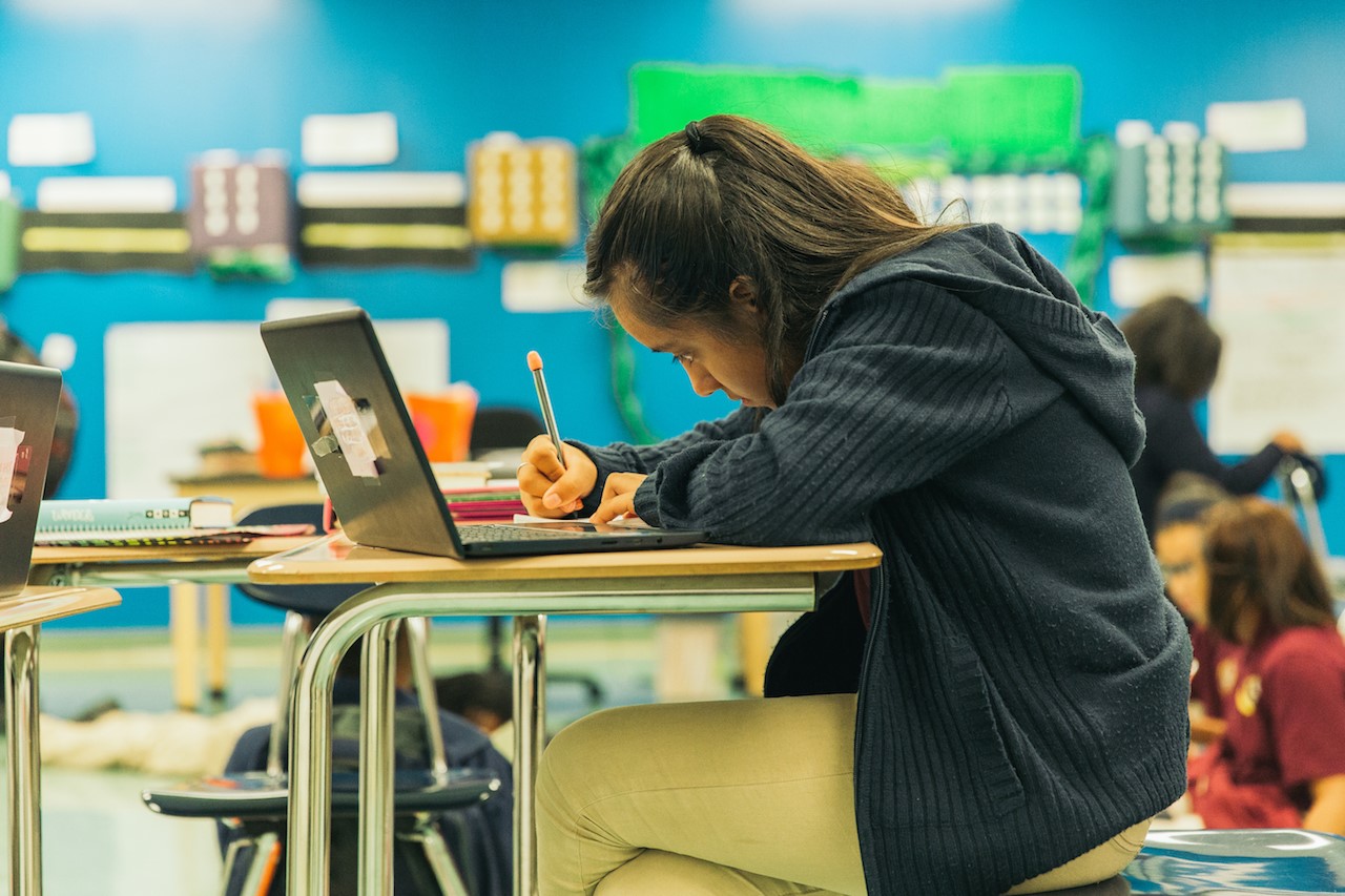 A student works diligently at her desk, her school-issued laptop not far from her reach. Photo by Noah Turley.