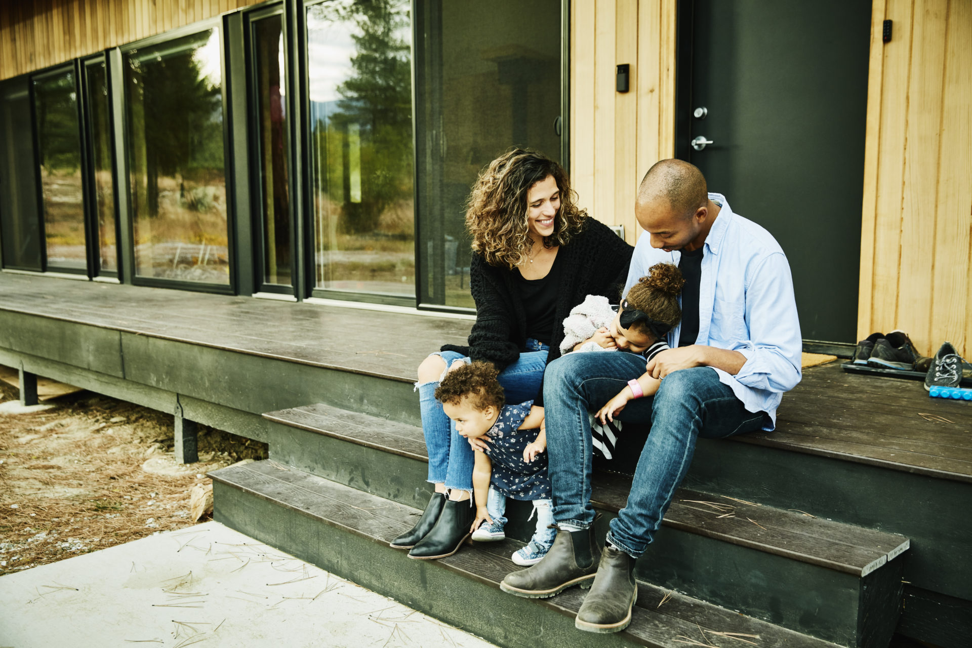 Smiling parents sitting with two young daughters on porch of cabin