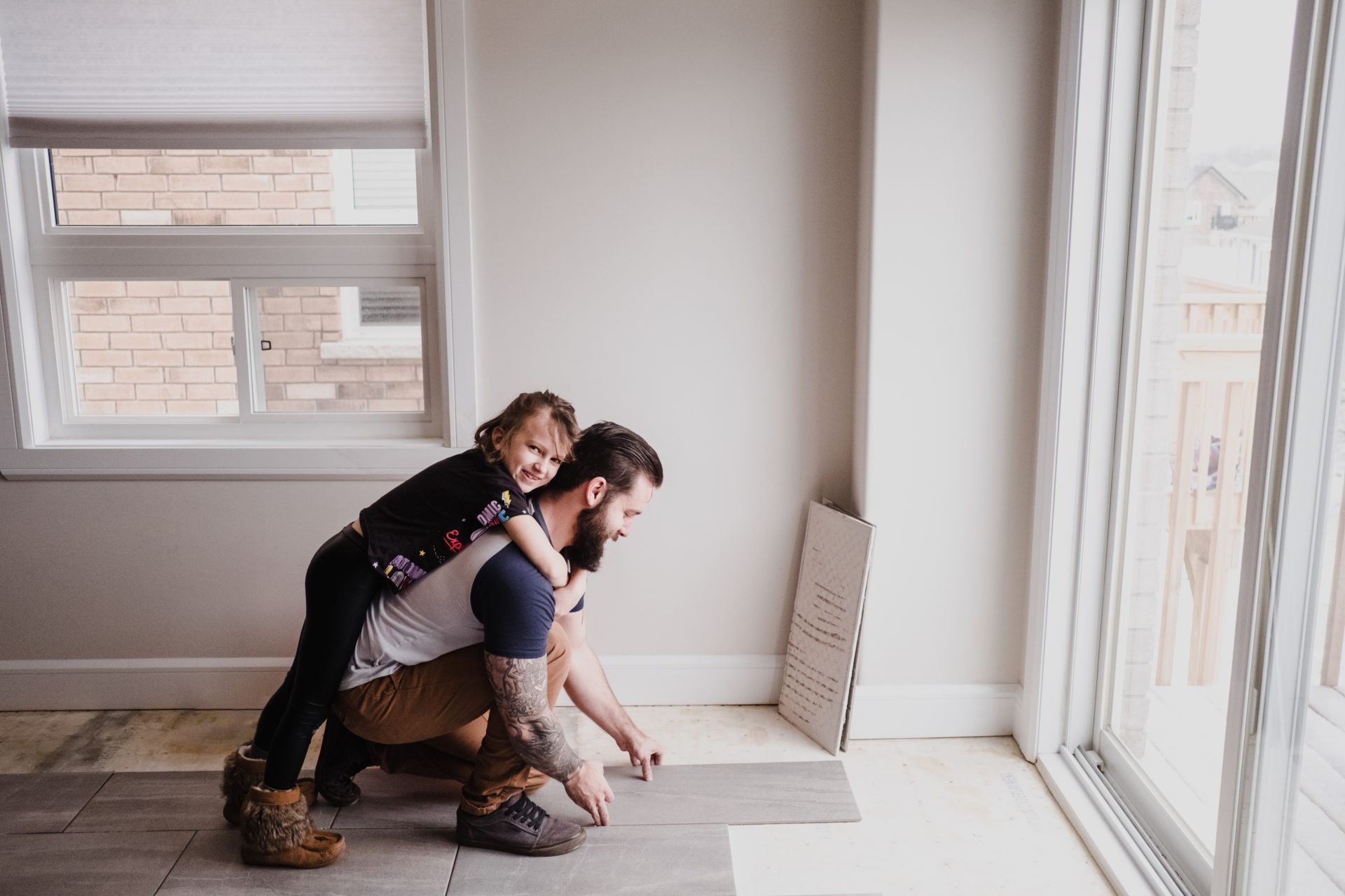 Girl hugging father installing floor tiles