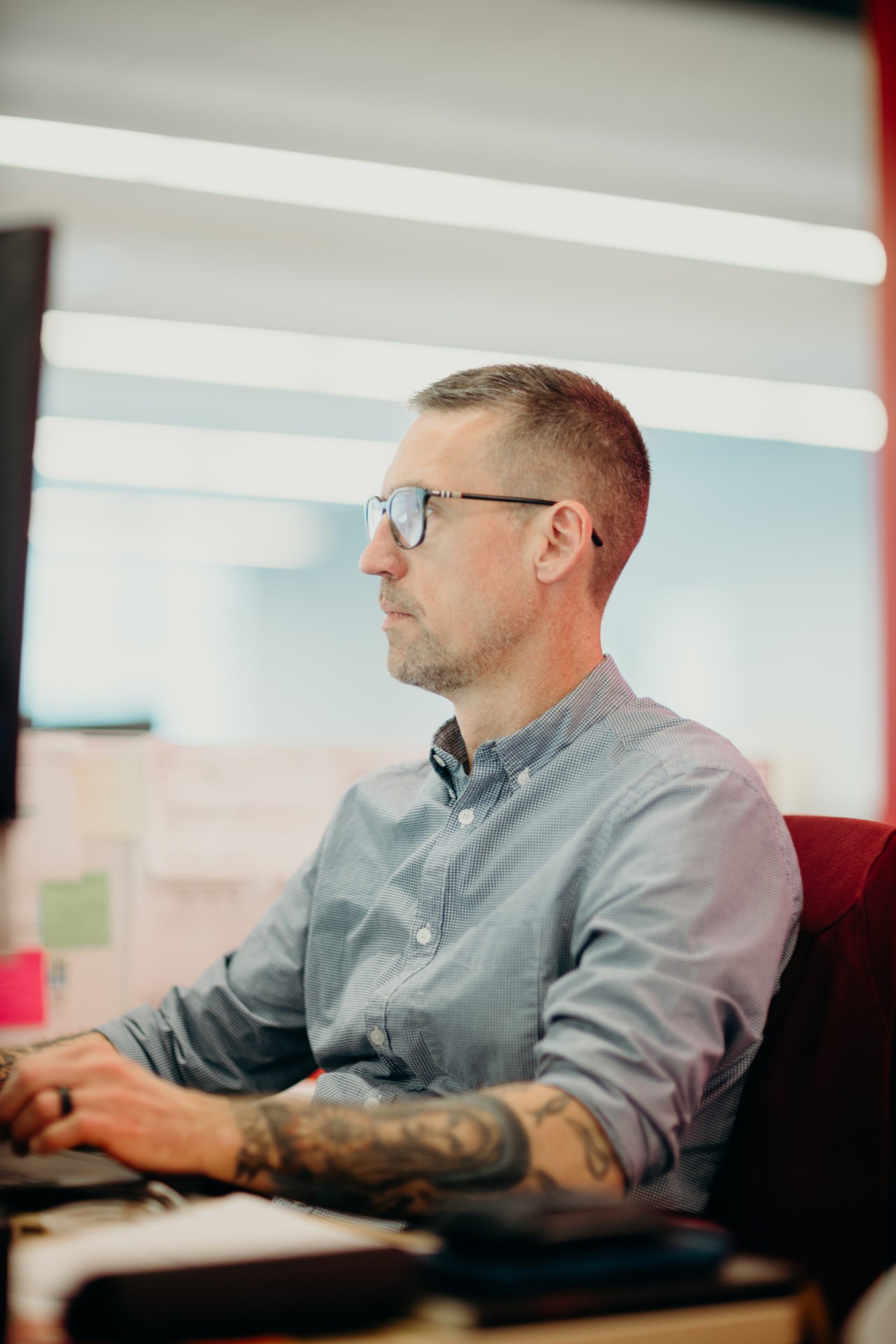 A man with tattoo and glasses working at his desk