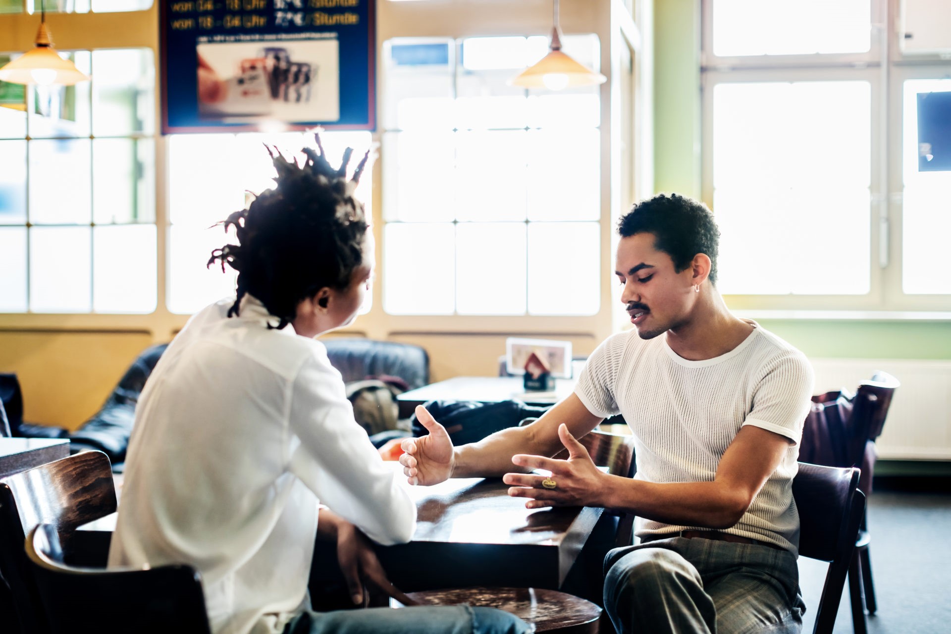 Couple Of Friends Sitting Down Chatting Together At Cafe