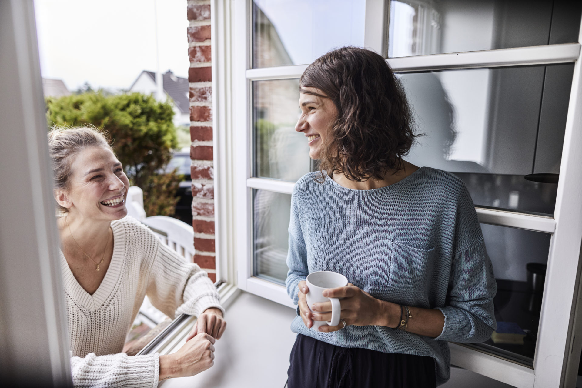 Two happy women talking through the window