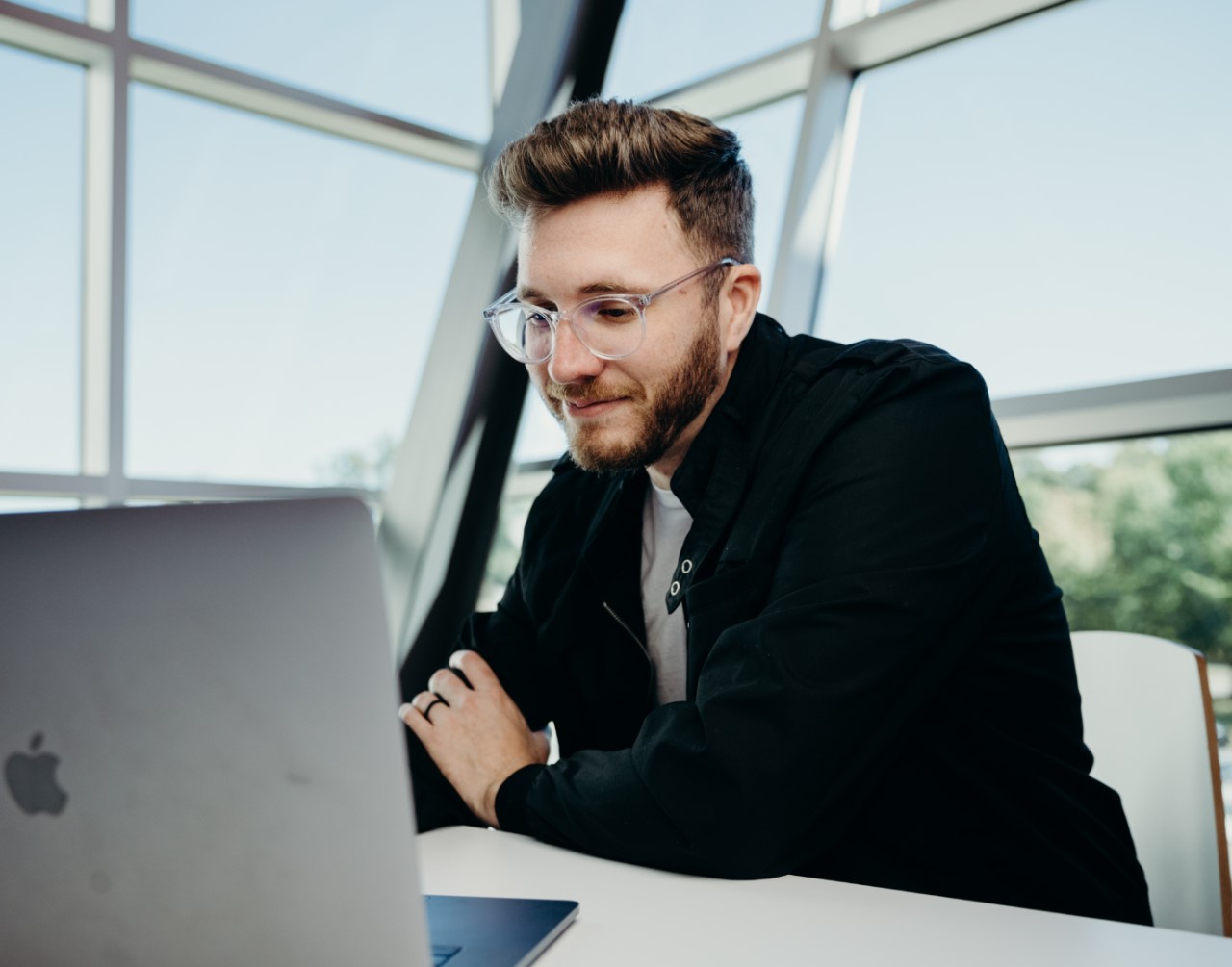 Man with glasses and black jacket working on a laptop