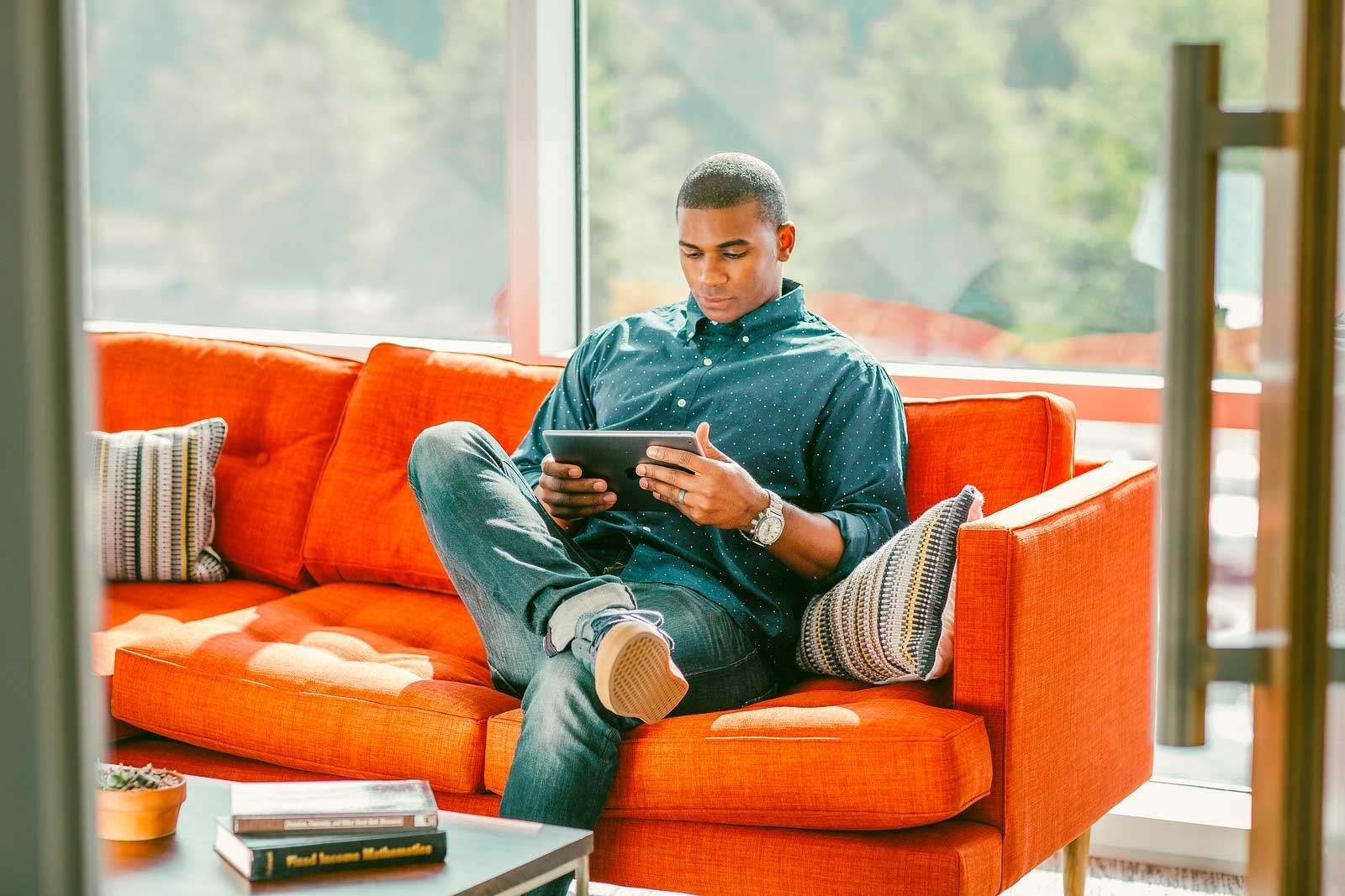 man sitting on orange couch reading from a tablet