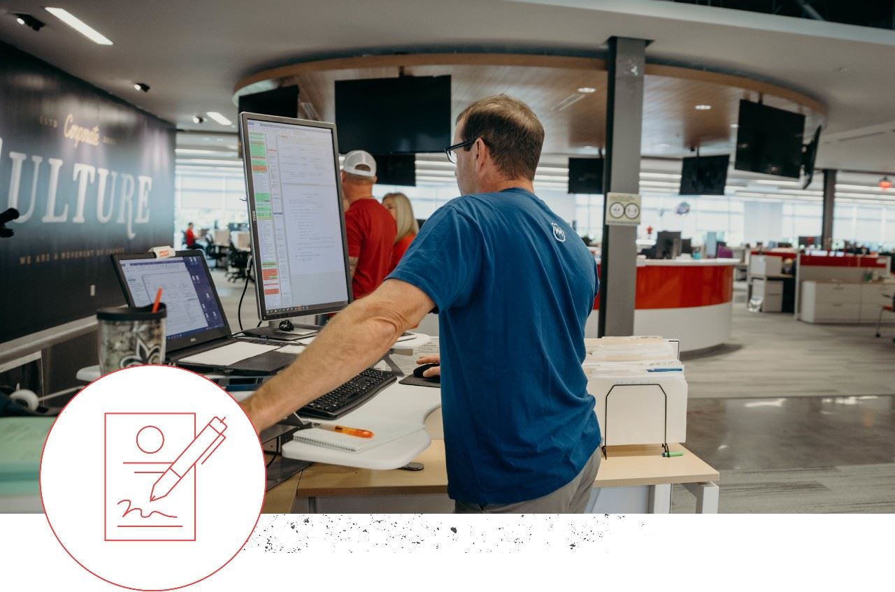 man working at a standing desk with icon in bottom left