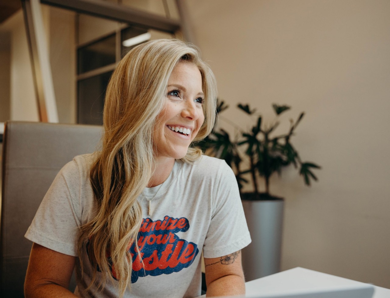 Woman seated at a table in front of a laptop looking off-camera and laughing