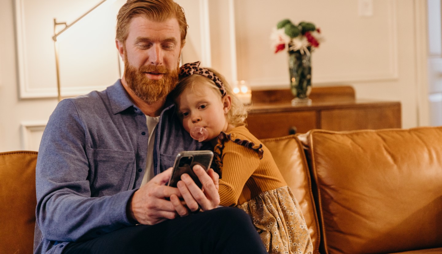 man and child sitting on a couch together looking at a mobile phone