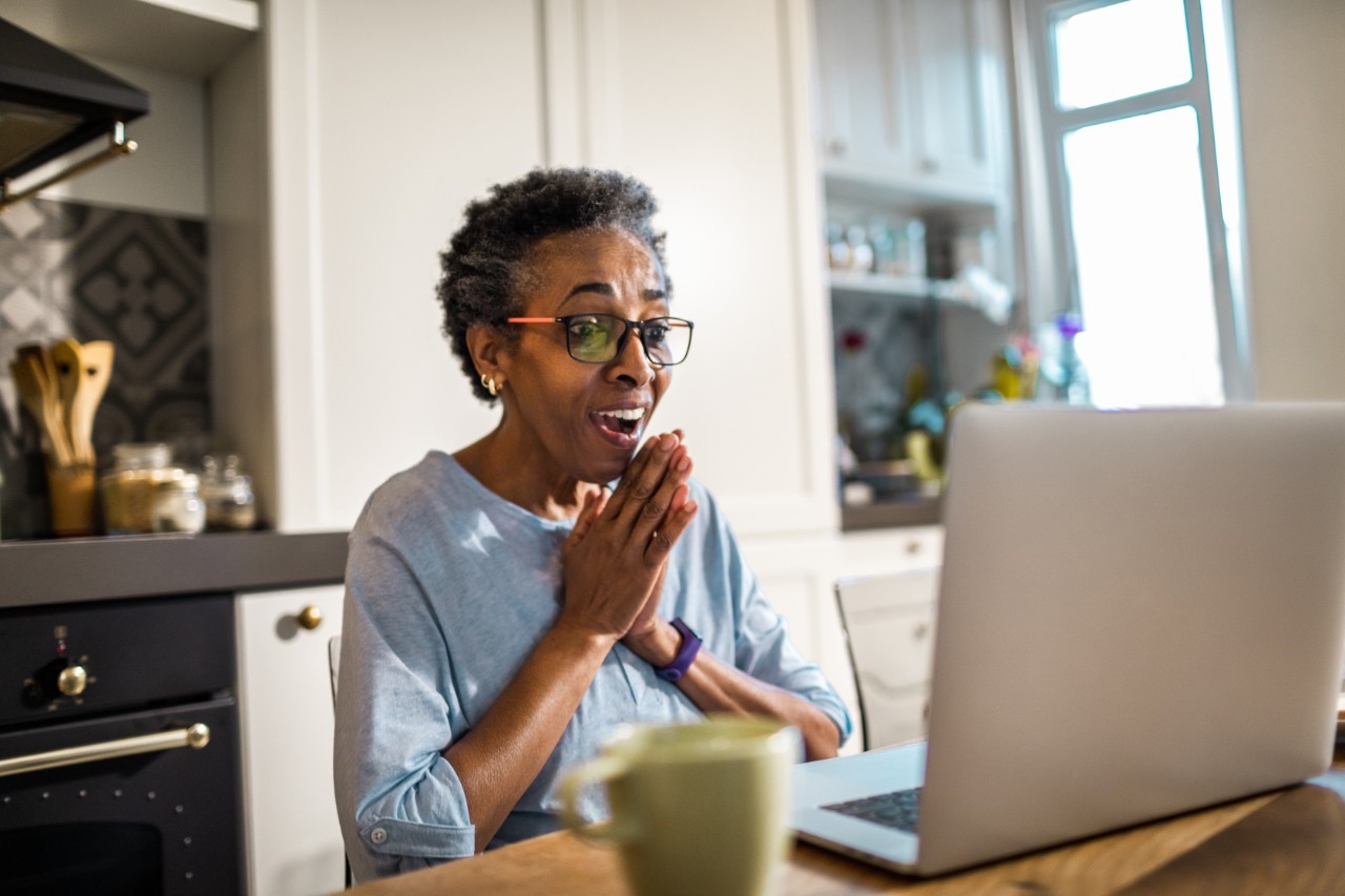 Black elderly woman excited while looking at her laptop in the kitchen